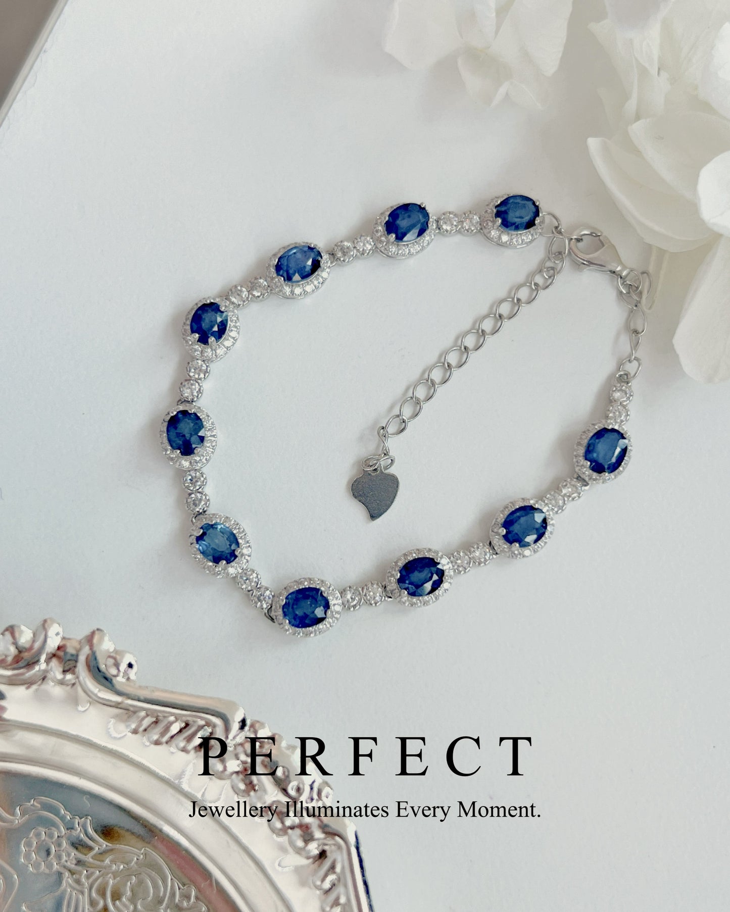 Silver bracelet with blue gemstones on a white surface with flowers.