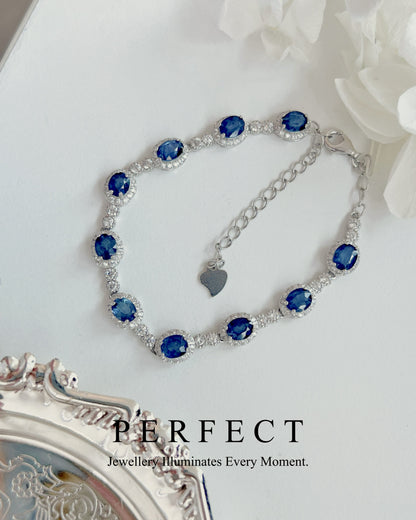 Silver bracelet with blue gemstones on a white surface with flowers.